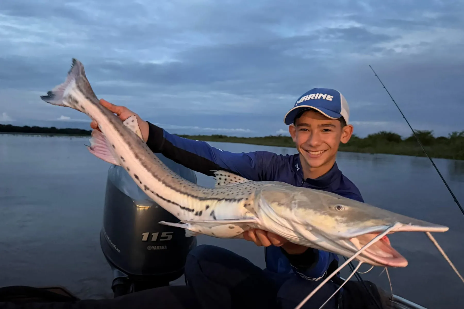 Jovem pescador segura um peixe de couro pintado no barco